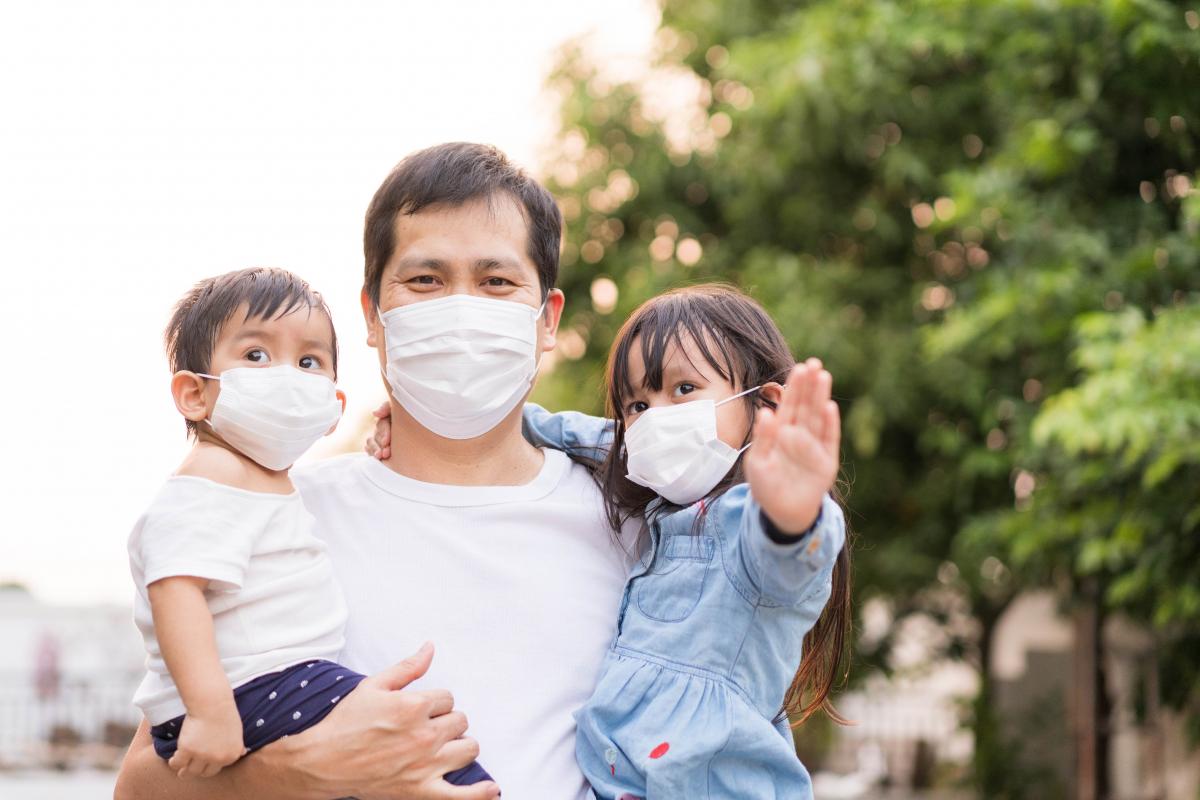 Dad in a mask holding his two young children also in masks