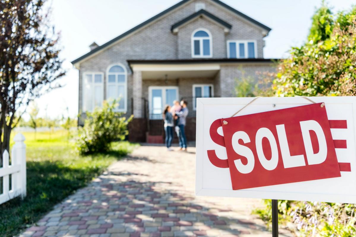 Family in front of home with a Sold sticker on the sign